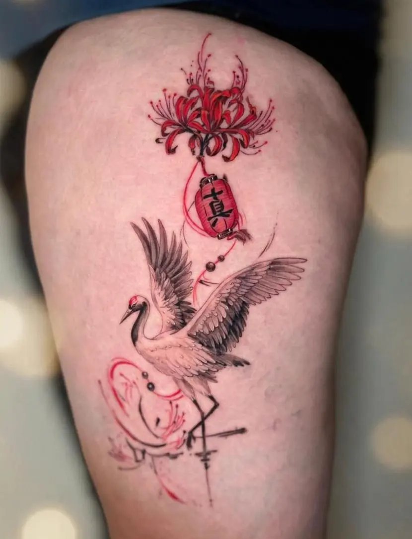Black crane with spread wings beneath a red spider lily and a red lantern, on a thigh.