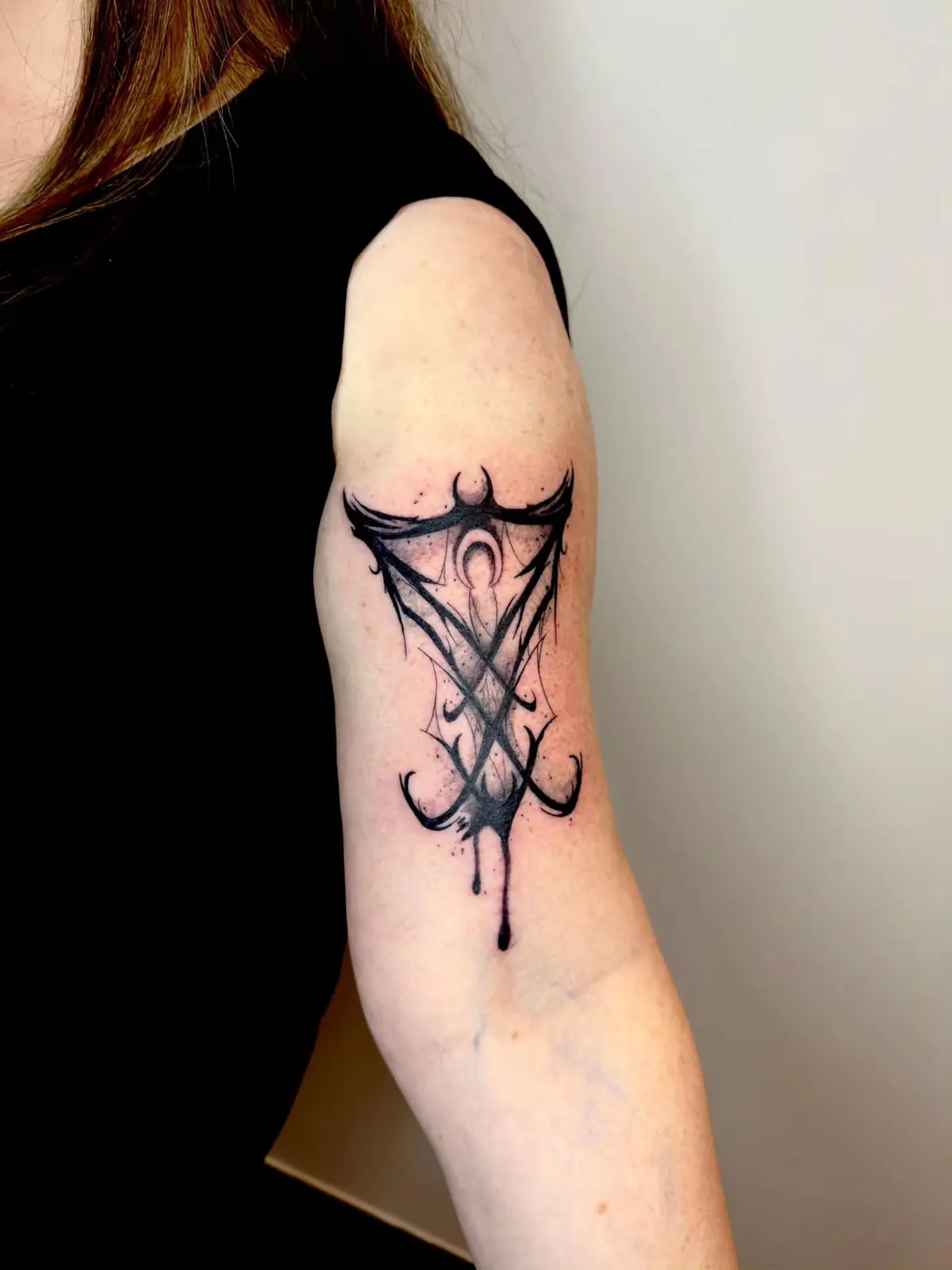 Symmetrical black occult sigil with dripping ink effect on the back of the upper arm.