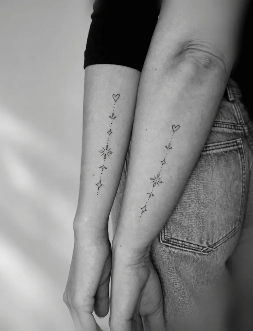 Two forearms side by side with matching vertical fine-line hearts and sparkles.