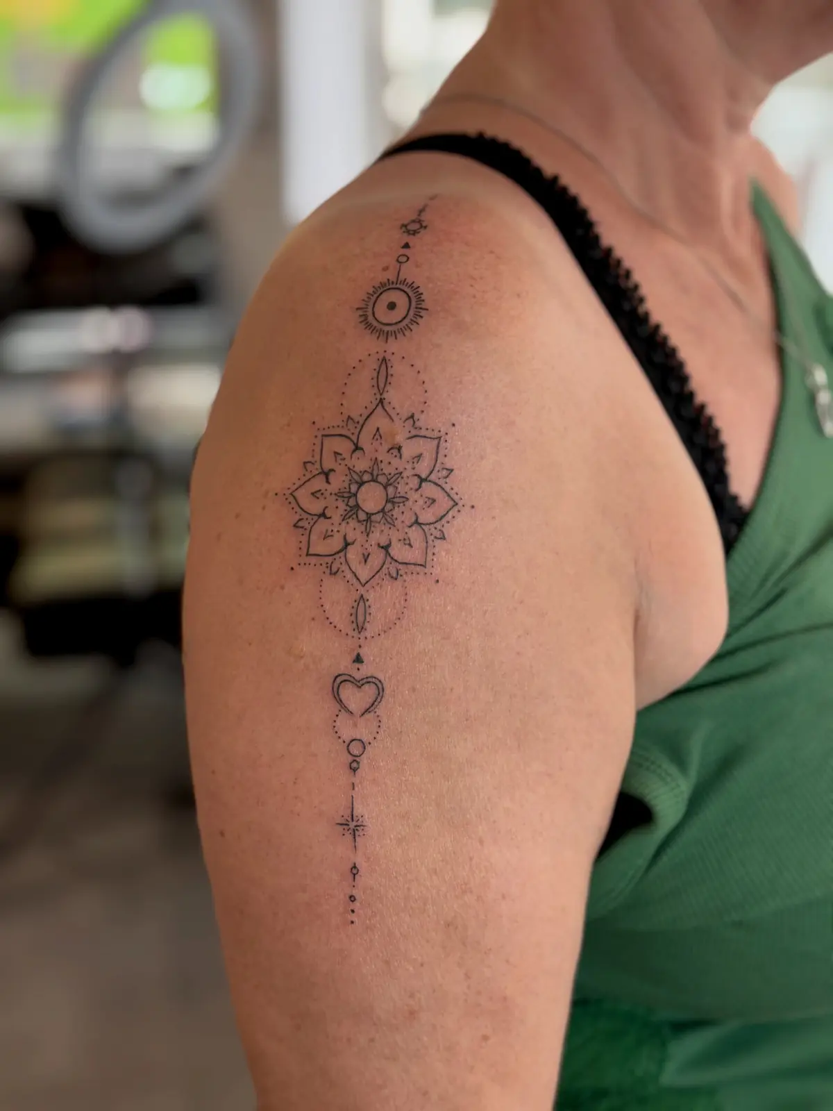 Fine dotwork mandala with a vertical ornamental chain of circles and a small heart running down the upper arm.