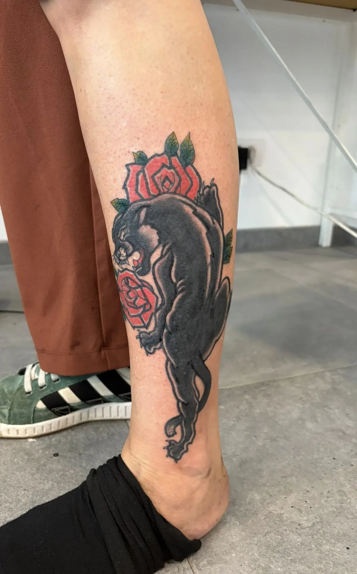 Traditional-style black panther climbing down the calf between two red roses with green leaves.
