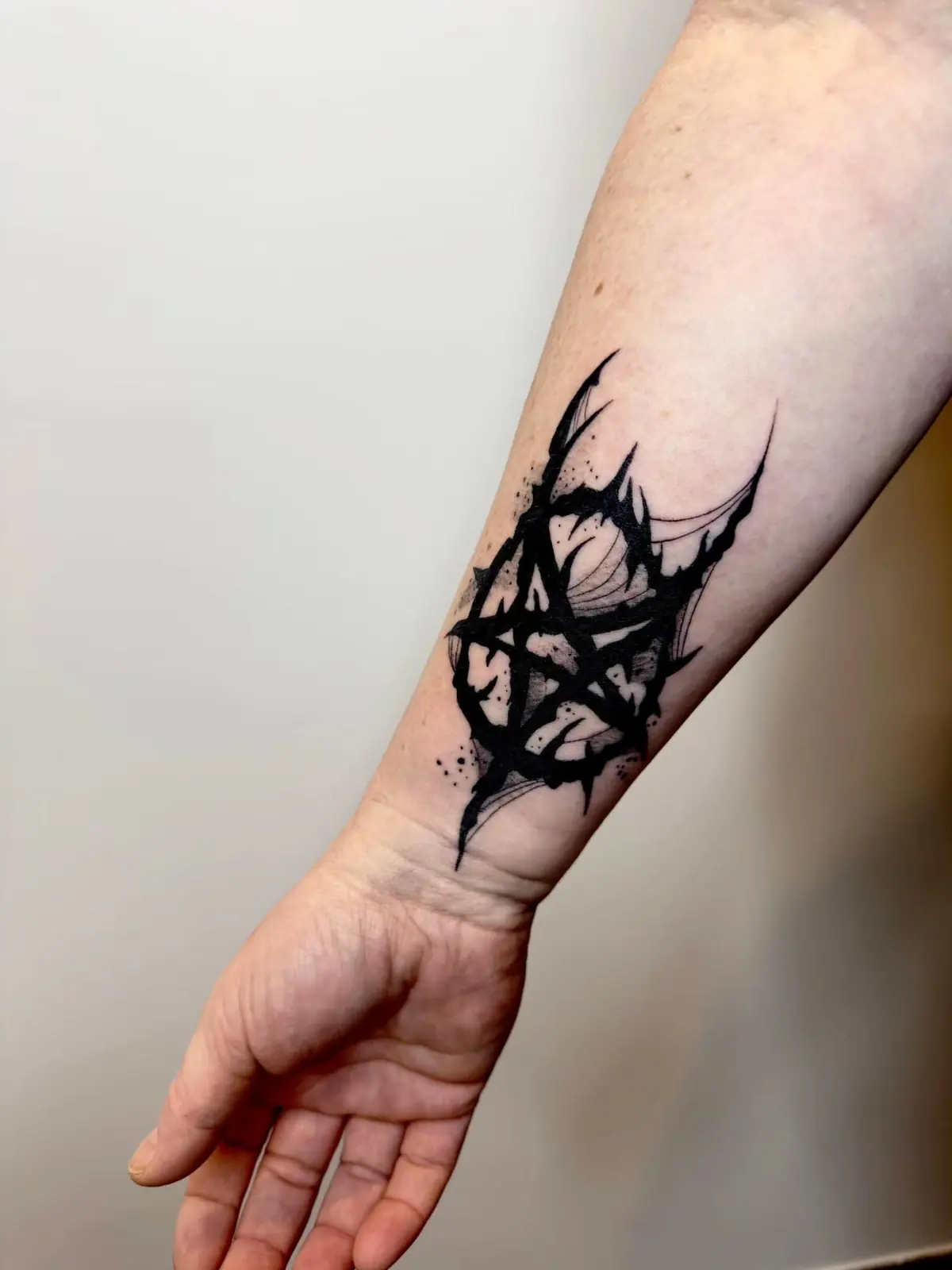 Bold black pentagram drawn in thorny, dripping brush strokes on the inner forearm.